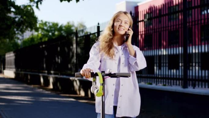 迷人的金发碧眼的女学生在她的电动踏板车上停下来，在电话上交谈，她笑得很大，感到非常兴奋。在阿里·阿列
