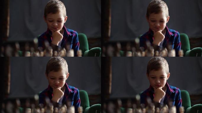 沉思的小男孩的特写肖像，正在思考坐在桌子上的棋盘上的下一步行动
