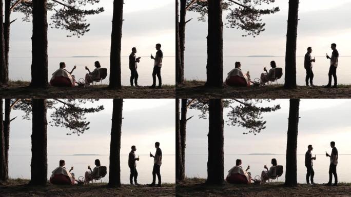 四个朋友在沙滩上休息。日落时在树下喝酒交流，玩得开心。