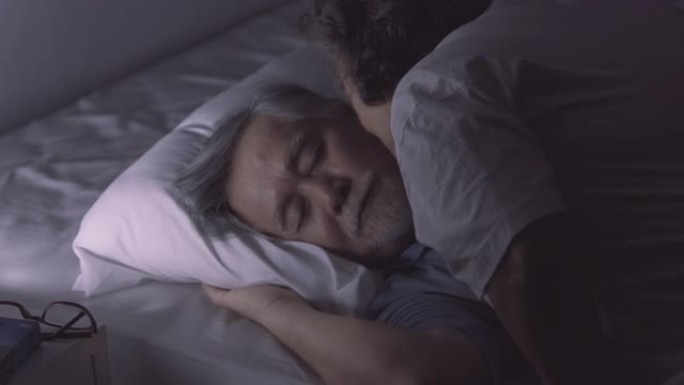老年男子睡在床上做梦，然后老年女子亲吻并在卧室睡觉时关灯