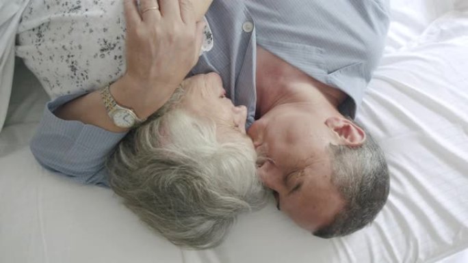 一对成熟夫妇一起躺在床上的高角度视图。他们拥抱着，男人亲吻着妻子的额头。