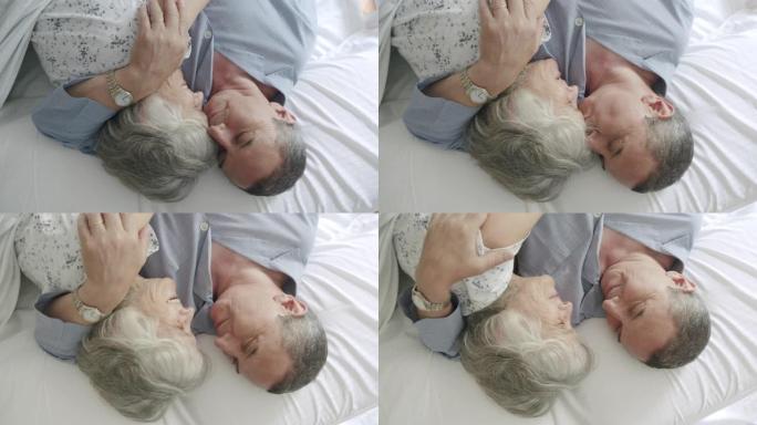 一对成熟夫妇一起躺在床上的高角度视图。他们拥抱着，男人亲吻着妻子的额头。