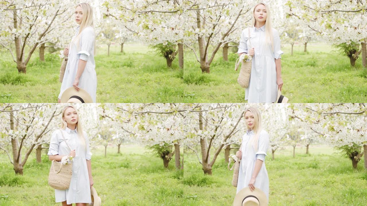 一个漂亮的金发女孩的肖像，穿着蓝色的裙子，一个草包和一顶帽子在一个盛开的樱桃花园。