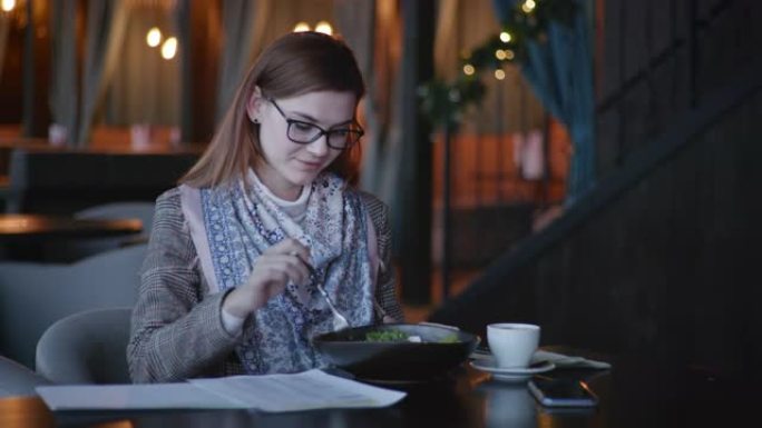 有眼镜的迷人年轻女子喜欢适当的营养在餐厅吃午餐，在卡路里表中检查新鲜蔬菜中的减肥蔬菜的热量，并写下饮