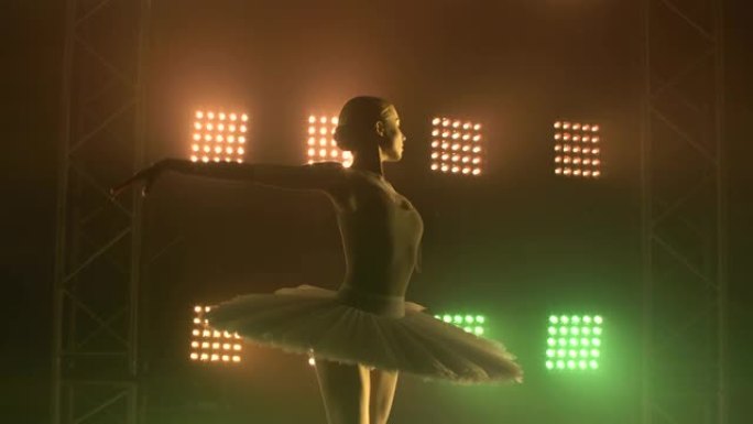 专业芭蕾舞演员在大舞台上在聚光灯下和烟雾中跳舞芭蕾舞。在泛光灯背景上穿着白色短裙的美丽年轻女孩的苗条
