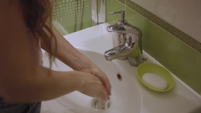 年轻的白人妇女在家里的水槽里洗手。室内洗手盆前的手特写。