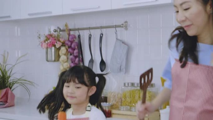 亚洲家庭母亲和女儿一起随着音乐跳舞，在家里的厨房里享受烹饪早餐，健康护理的日常活动理念