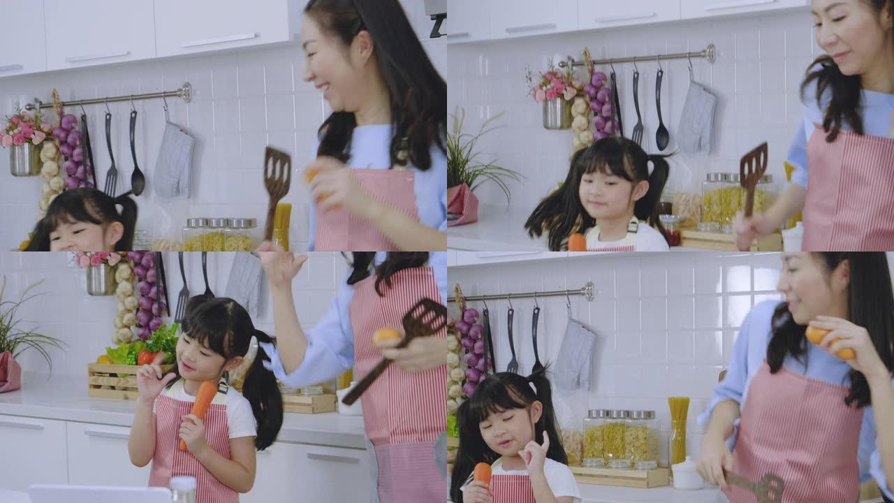 亚洲家庭母亲和女儿一起随着音乐跳舞，在家里的厨房里享受烹饪早餐，健康护理的日常活动理念