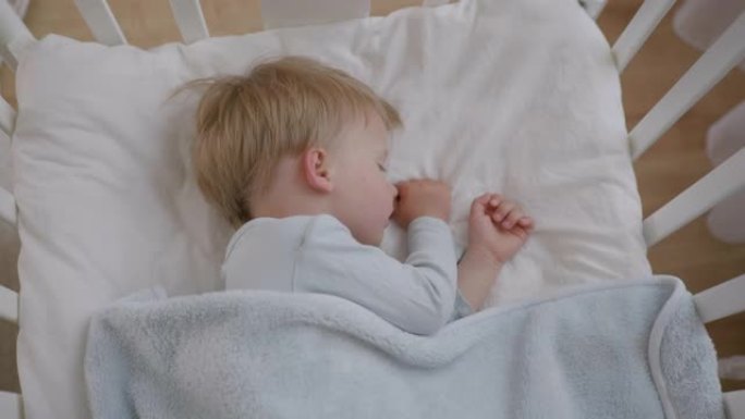 小有吸引力的婴儿白天在房间的婴儿床里用毯子覆盖的柔软舒适的枕头上睡得很香