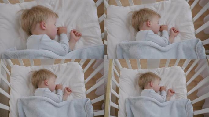 小有吸引力的婴儿白天在房间的婴儿床里用毯子覆盖的柔软舒适的枕头上睡得很香
