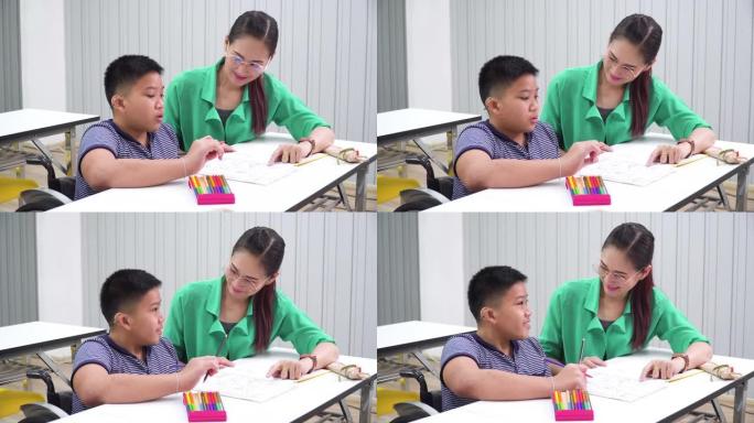 一个耳朵残疾的少年坐在轮椅上问问题，做作业，在教室里和一位美丽的亚洲老师一起完成作业。这个男孩坐在桌