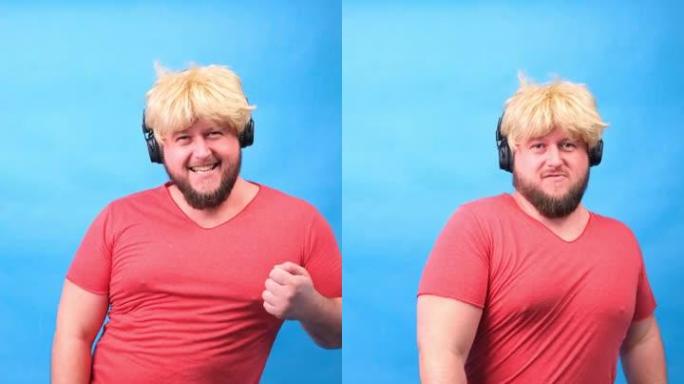 戴着耳机和戴着粉色t恤的假发的滑稽胖乎乎的男人在蓝色背景上跳舞和大笑，垂直