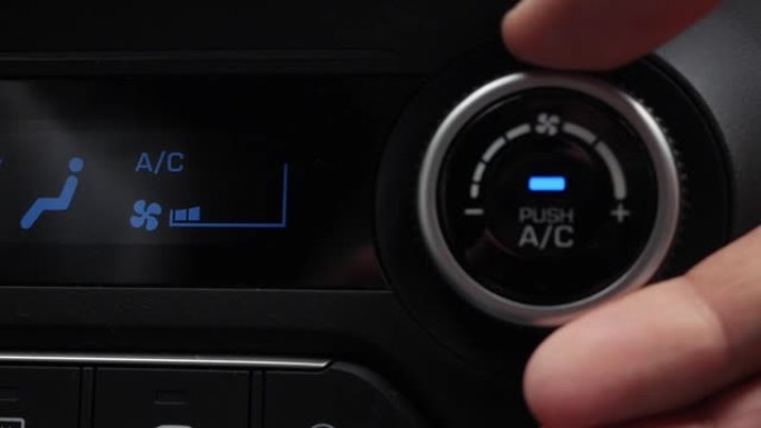 按下按钮打开汽车空调的特写镜头。男人的手转动按钮，调节车内的舒适性