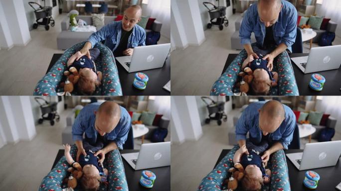年轻的随便穿衣服的单身父亲在大流行期间在家工作时与他的男婴玩耍