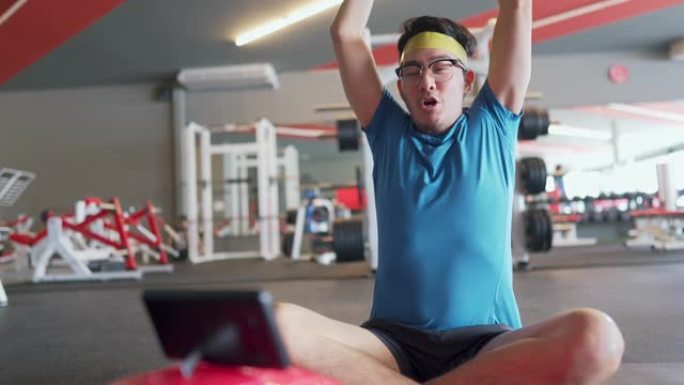 亚洲瘦男人在健身房锻炼时用智能手机看喜剧电影