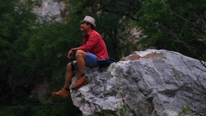男人坐在岩石悬崖上喝啤酒。
