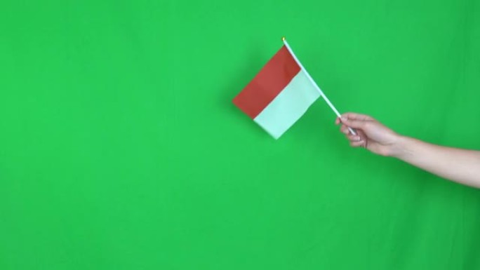 在演播室的绿色背景上，一只不知名的手举着一面印度尼西亚国旗。4k分辨率拍摄