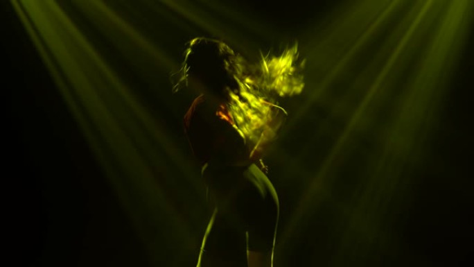 一个年轻女孩活泼的剪影在一个黑暗的工作室里用蓝光跳舞时髦的爵士乐。特写