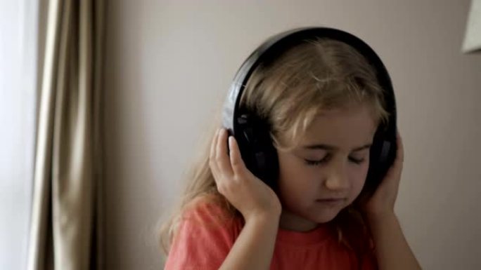 漂亮可爱的快乐小女孩用无线耳机听音乐。有趣的小女孩跳舞，唱歌，移动节奏。戴着耳机的孩子。特写。家居休