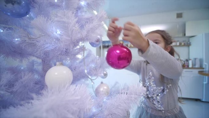 4k视频，小黑发女孩在家里的人造圣诞树上悬挂一个粉色玻璃摆设。
