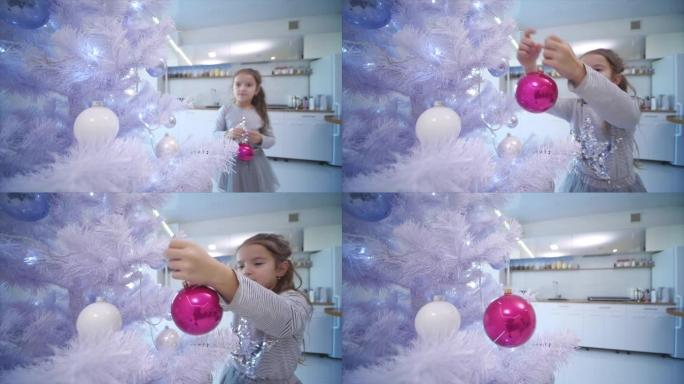 4k视频，小黑发女孩在家里的人造圣诞树上悬挂一个粉色玻璃摆设。