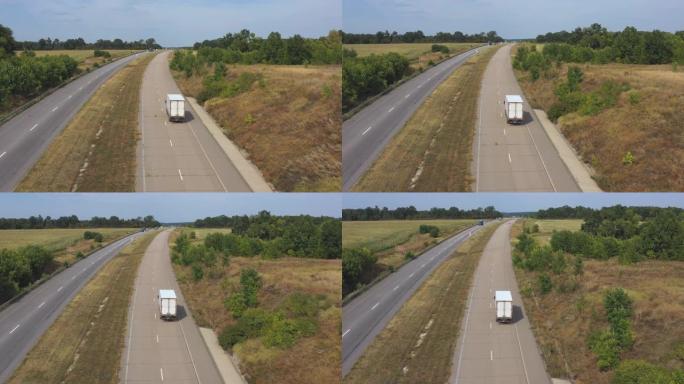 在高速公路上行驶并运输货物的卡车与货运拖车的空中射击。在晴天通过乡村高速公路行驶的送货卡车的摄像头。