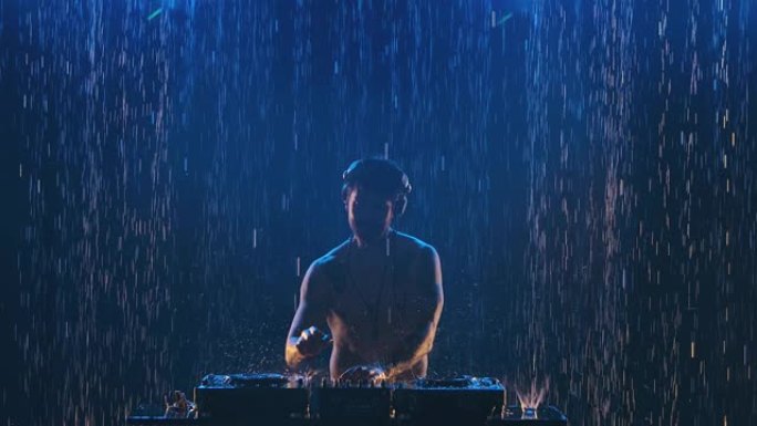 专业耳机中的性感男性dj在控制面板上播放，用于在黑暗的工作室中混合音乐。雨中闪烁着轮廓的身体，上面布