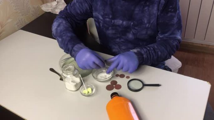 一个戴着口罩和橡胶手套的人用苏打水和水稀粥擦拭铜币。附近有清洗铜币的磷酸和硫酸软膏。