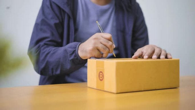 快速后发货服务理念。年轻的亚洲男子客户在家庭办公桌上的包裹纸板箱上写地址。4k分辨率。