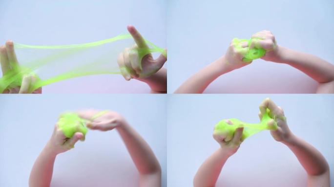 女孩把绿色粘液伸向两边。孩子们玩粘液玩具的手。在白色上制作粘液。时髦的液体玩具粘在手上和手指上。4k
