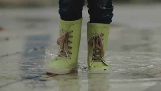 雨中，穿着橡胶靴的小男孩站在水坑里