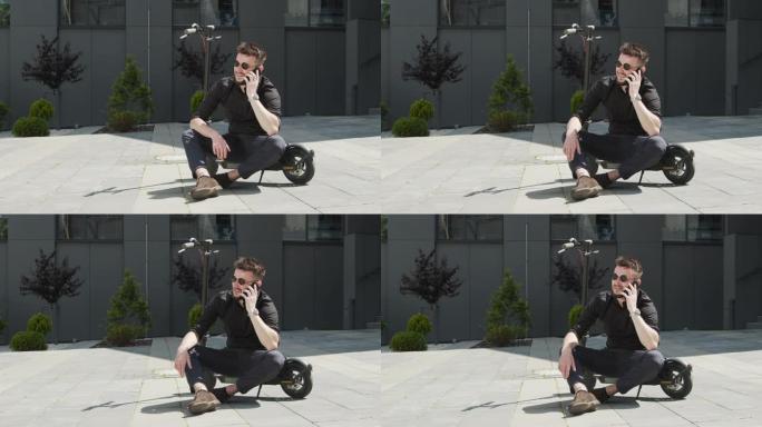 一名男学生坐在街中央的电动踏板车上，用手机聊天。戴着黑色眼镜的白人男子骑着电动滑板车。
