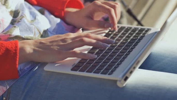 新鲜空气中的女孩在白色笔记本电脑的键盘上打字。年轻老练的女人在户外使用笔记本电脑