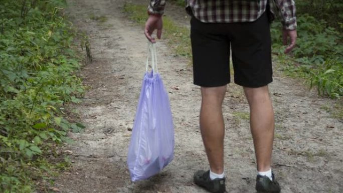 一个坏人从森林里的塑料垃圾袋里扔垃圾。雄性入侵者留下垃圾并走开。污染和生态问题，塑料回收，自然污染