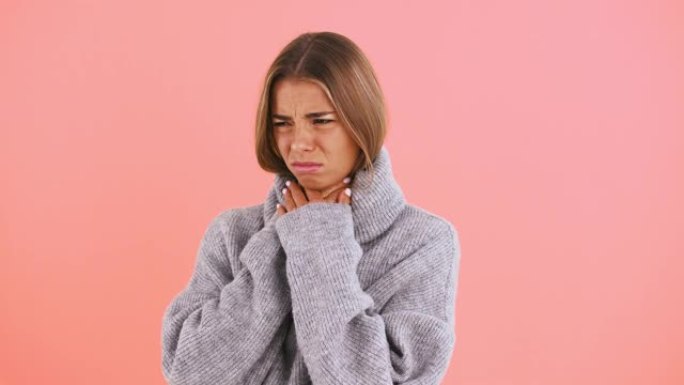 女性喉咙痛和咳嗽，在粉红色的工作室背景下摆姿势时看起来不开心和生病