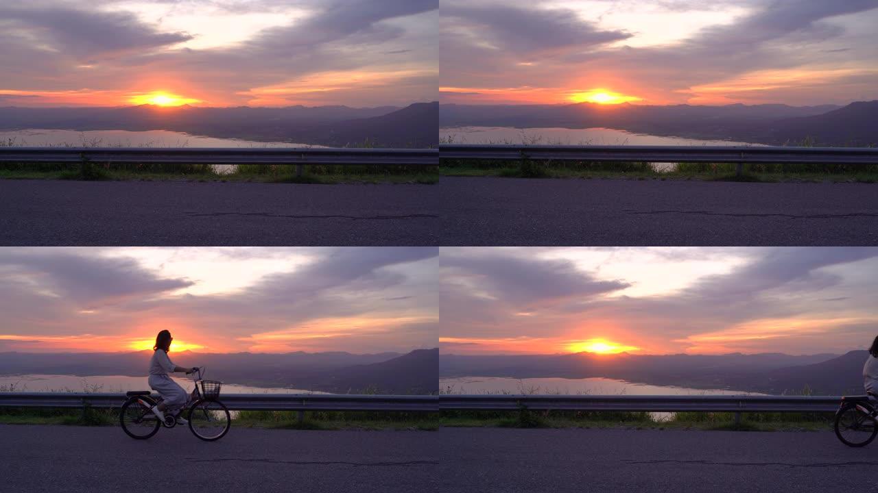 亚洲女子骑自行车看夕阳山山背景美景旅游休闲活动理念