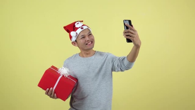 亚洲泰国男子用智能手机直播并在黄色背景上拿着红色礼盒