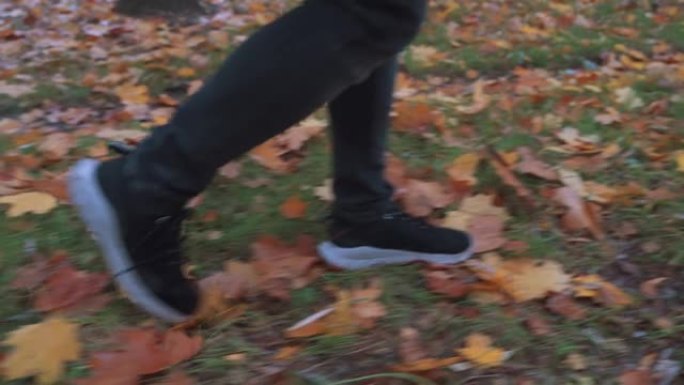 穿着运动鞋和黑色紧身牛仔裤踢黄色和橙色秋叶的男人的侧视图。慢动作。秋季概念