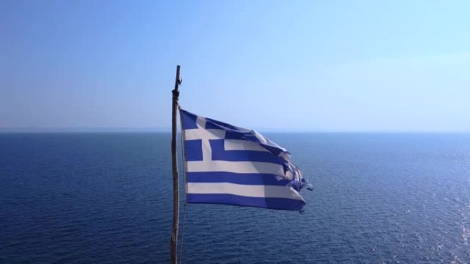 希腊国旗在风中飘扬，后面是蔚蓝的大海
