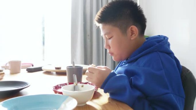 穿着蓝色兜帽的快乐亚洲男孩在上学前早上和妹妹一起吃早餐。