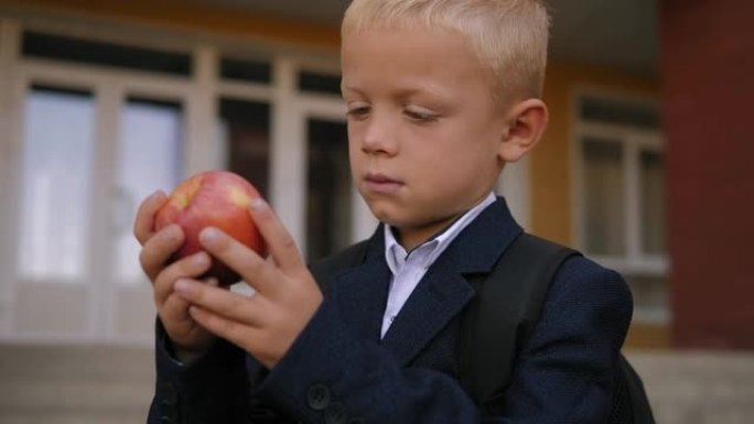 一个男孩的特写镜头，背包里有一个苹果站在学校附近。