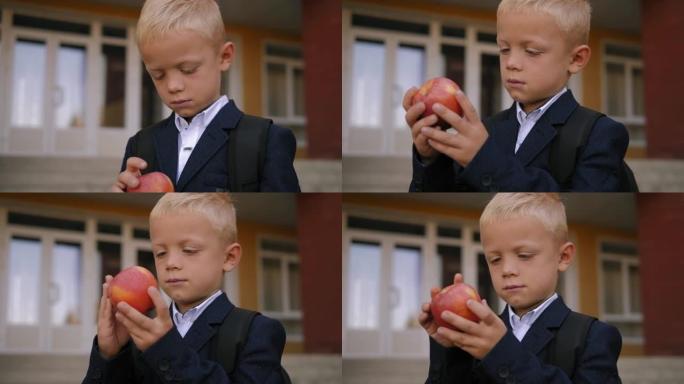 一个男孩的特写镜头，背包里有一个苹果站在学校附近。