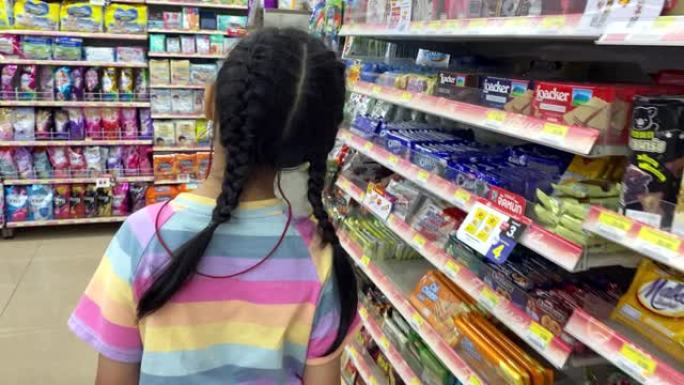 亚洲女孩戴着口罩，在杂货店寻找小吃