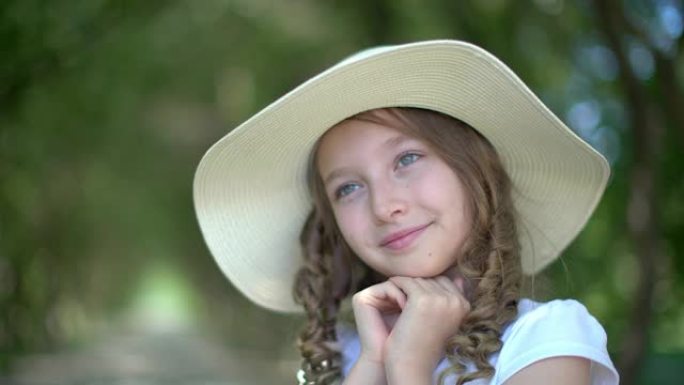 可爱的女孩肖像，戴着白帽子，双手紧握着绿色花园的脸。可爱的年轻的夏天帽子女孩微笑着，在夏天的公园里向