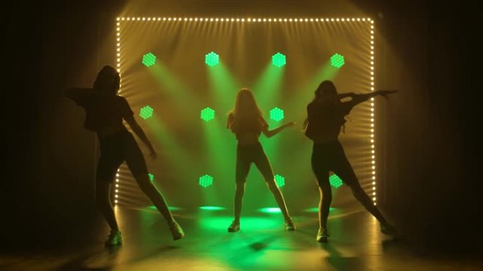 穿着运动服跳舞的女孩组成的舞蹈团爵士放克舞。在绿色灯光背景下的黑暗工作室中，三个女孩的剪影。慢动作