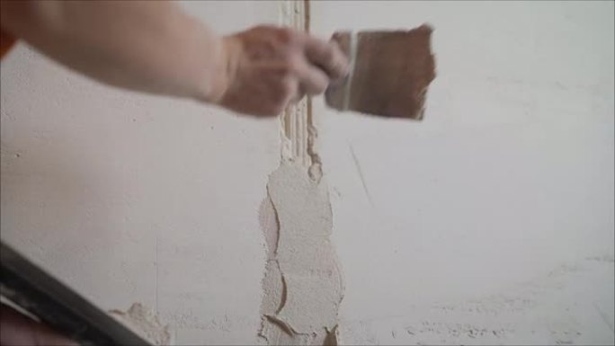 工人盖住不平坦的墙壁，用大铲和油灰将人的手盖上，进行公寓维修。工人用油灰处理墙壁。