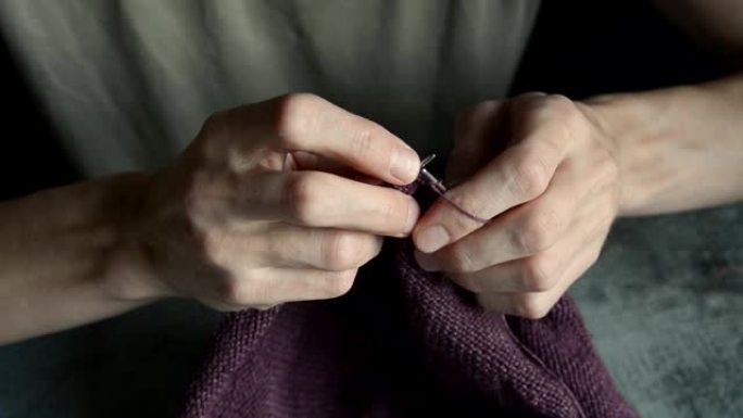 成年年轻人用灰色金属针和深红色棉线编织手