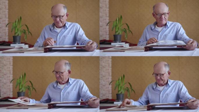 开朗的老人享受着家庭相册的记忆，坐在桌子旁的房间里看着旧照片