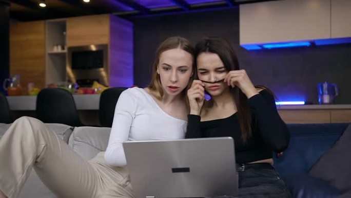 迷人的微笑快乐的25岁女性朋友的前视图，他们一起用电脑度过了共同的空闲时间，坐在现代房间的工作室里