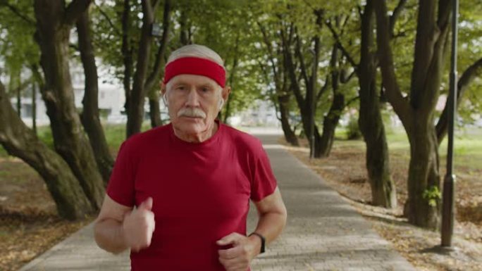 在公园里沿路跑的男性老人。成熟的跑步者训练，听音乐